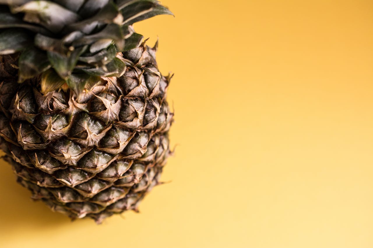 A close-up of a fresh pineapple against a vibrant yellow background, showcasing its texture.