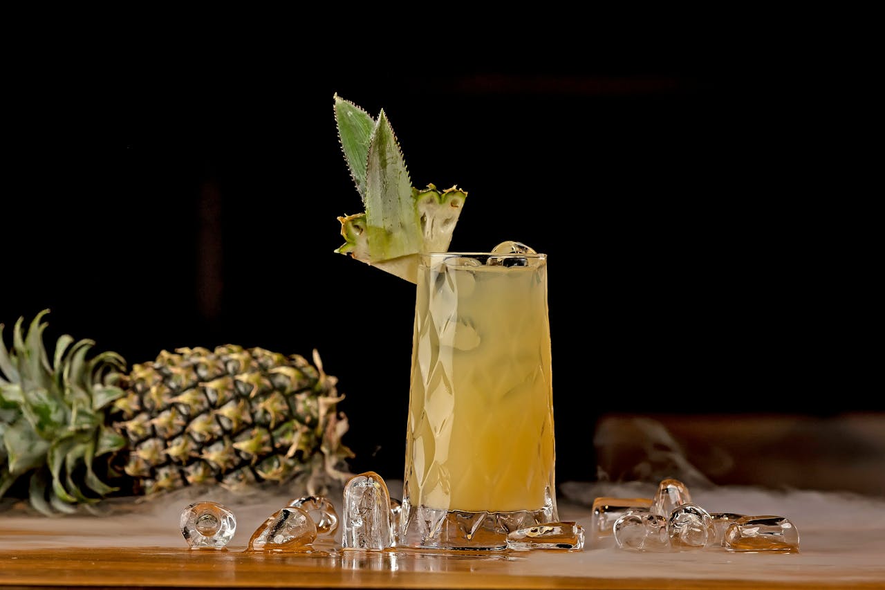 Cool pineapple cocktail with ice, garnished with a slice, on a wooden surface.
