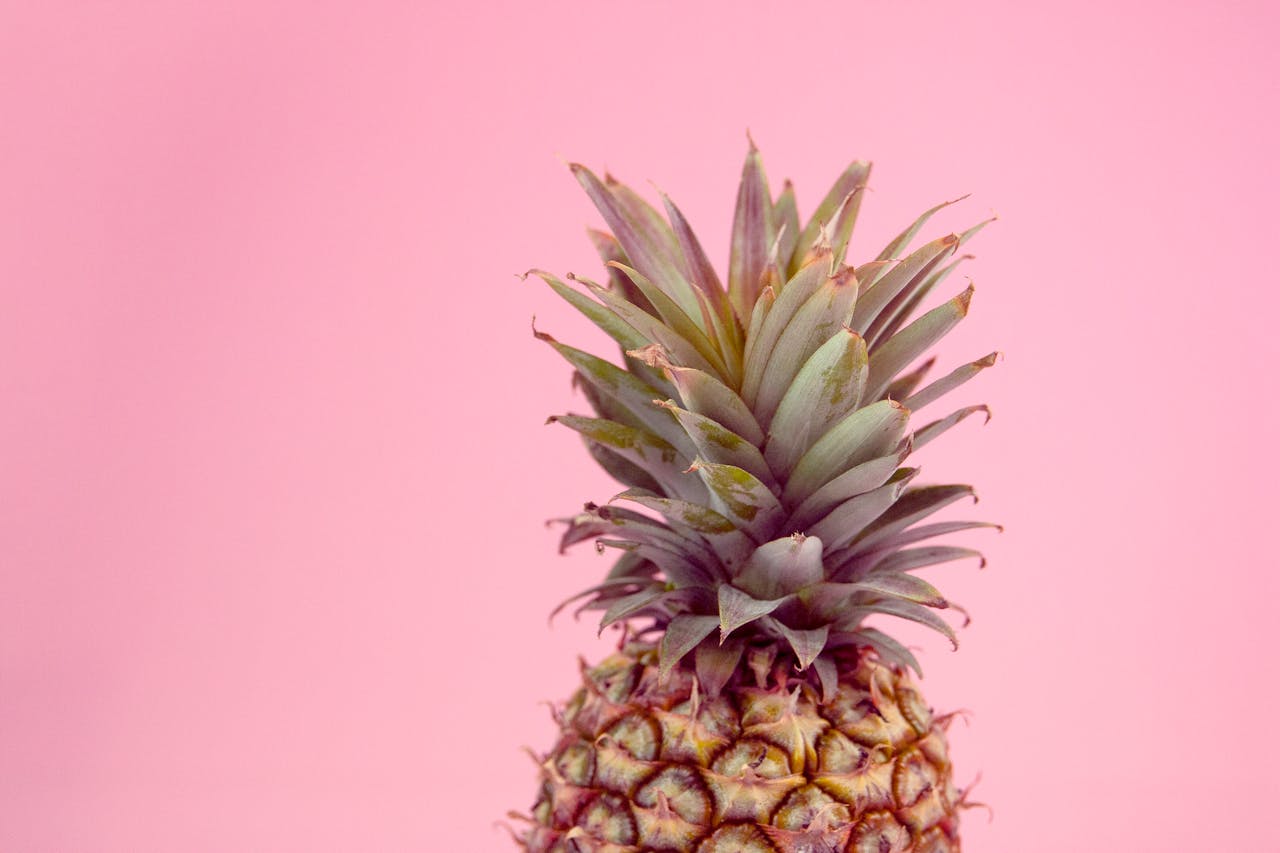 Vivid close-up of a pineapple against a pink background, showcasing tropical freshness.